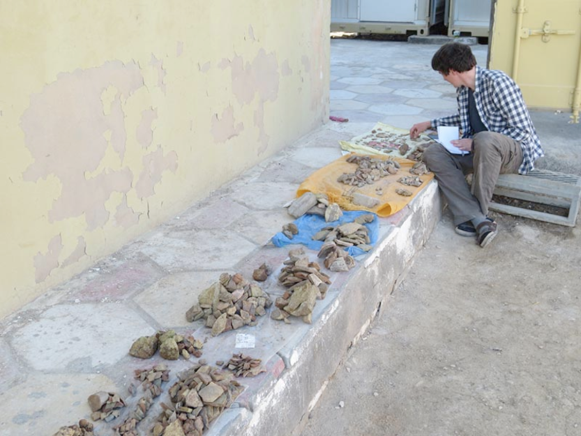 The author sits on a stone step and sorts through piles of sherds at the dig site