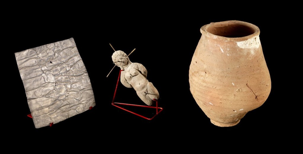 A assemblage of three items with magical connotations, including a lead curse tablet, a clay doll pierced by spike, and the ceramic jar in which they were placed. 
