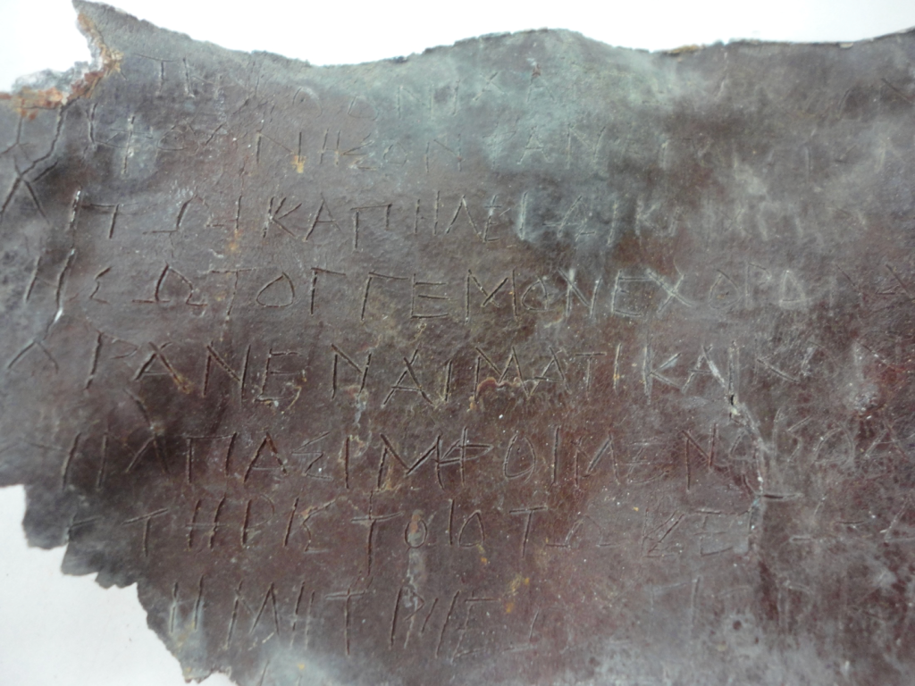 A reddish-grey lead sheet with Ancient Greek writing on it. 