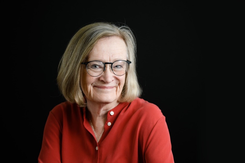 Image of Dr Elizabeth D. Carney, a white woman with shoulder length straight blond hair. She wears black circular glasses and a red long sleeve shirt. 