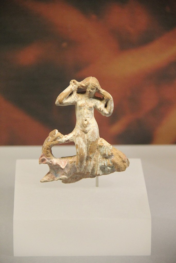 A small terracotta figurine of a naked woman rising from the sea, holding her hair out with both hands